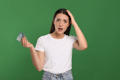 Shocked woman with credit card on green background. Debt problem