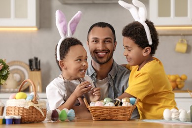 Photo of Happy African American father and his cute children with Easter eggs at table in kitchen