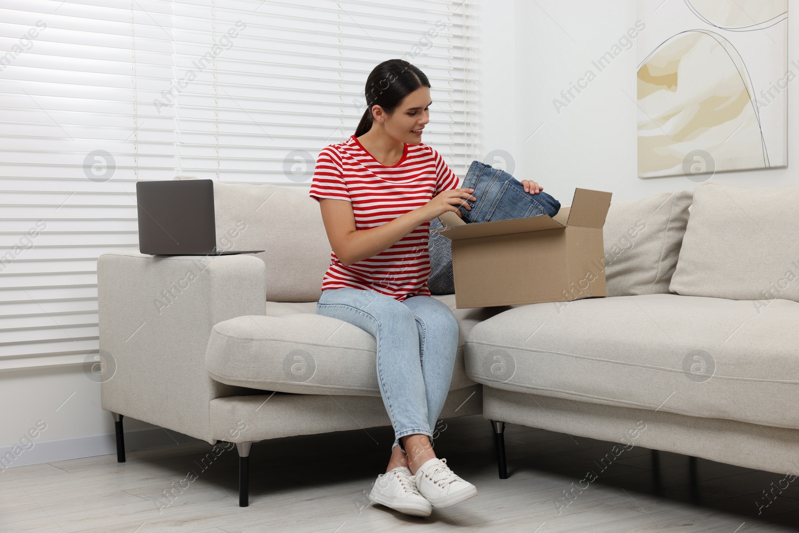 Photo of Young woman with just unpacked new jeans on sofa at home. Online shopping