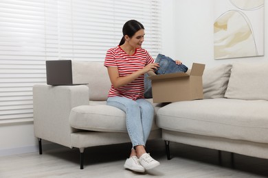 Young woman with just unpacked new jeans on sofa at home. Online shopping