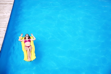 Young woman on inflatable mattress in swimming pool, above view