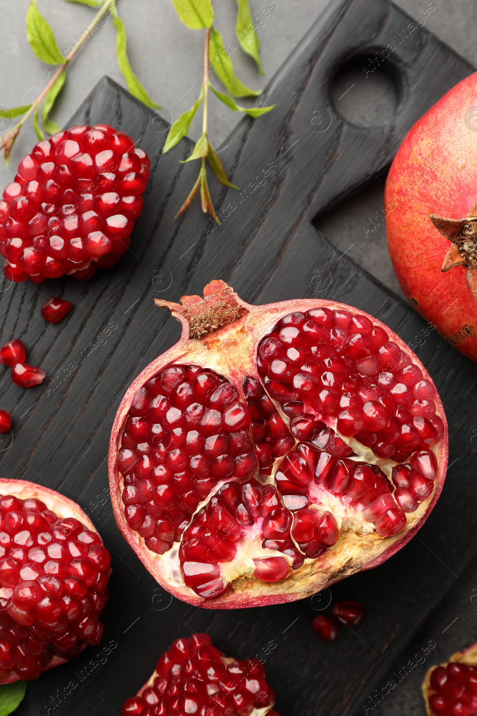 Photo of Cut fresh pomegranate and green leaves on grey table, top view