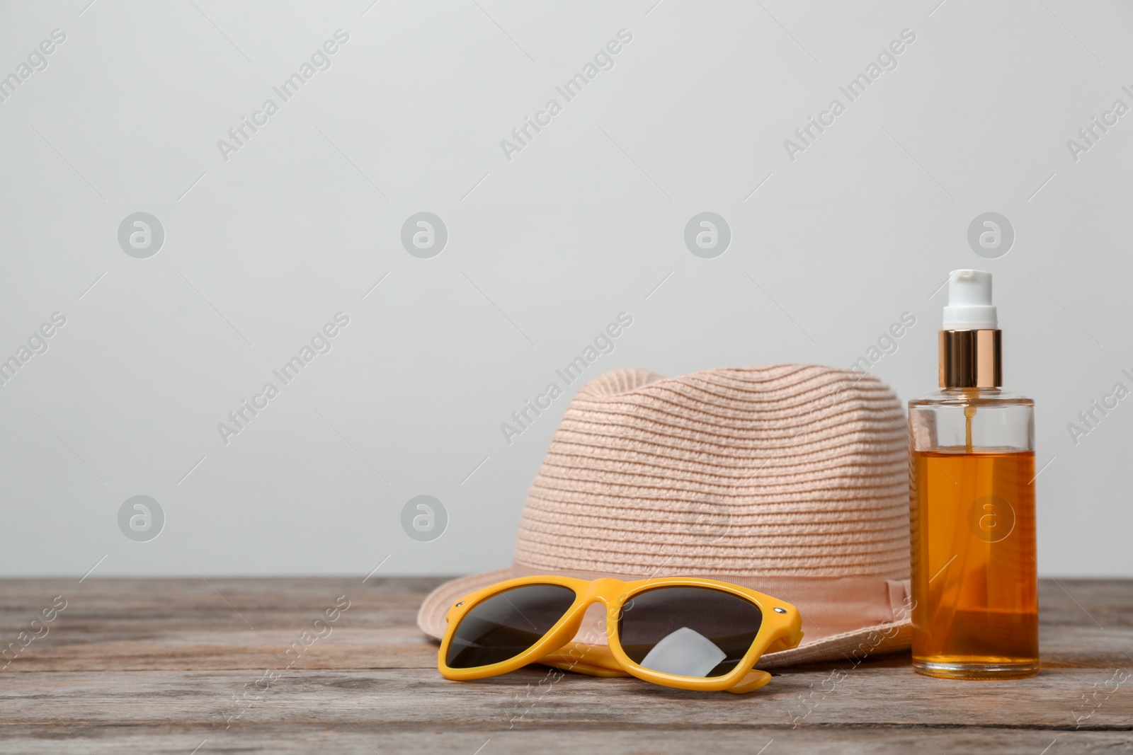 Photo of Hat, sunglasses and bottle with sun oil on wooden table against light background. Beach objects