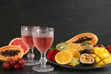 Delicious exotic fruits and glasses of wine on black table