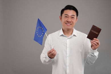 Immigration. Happy man with passport and flag of European Union on grey background, space for text