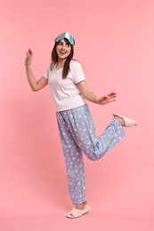 Happy woman in pyjama and sleep mask on pink background