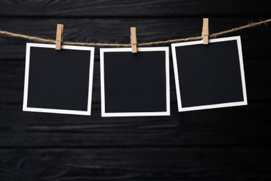 Photo of Clothespins with empty instant frames on twine against black wooden background. Space for text