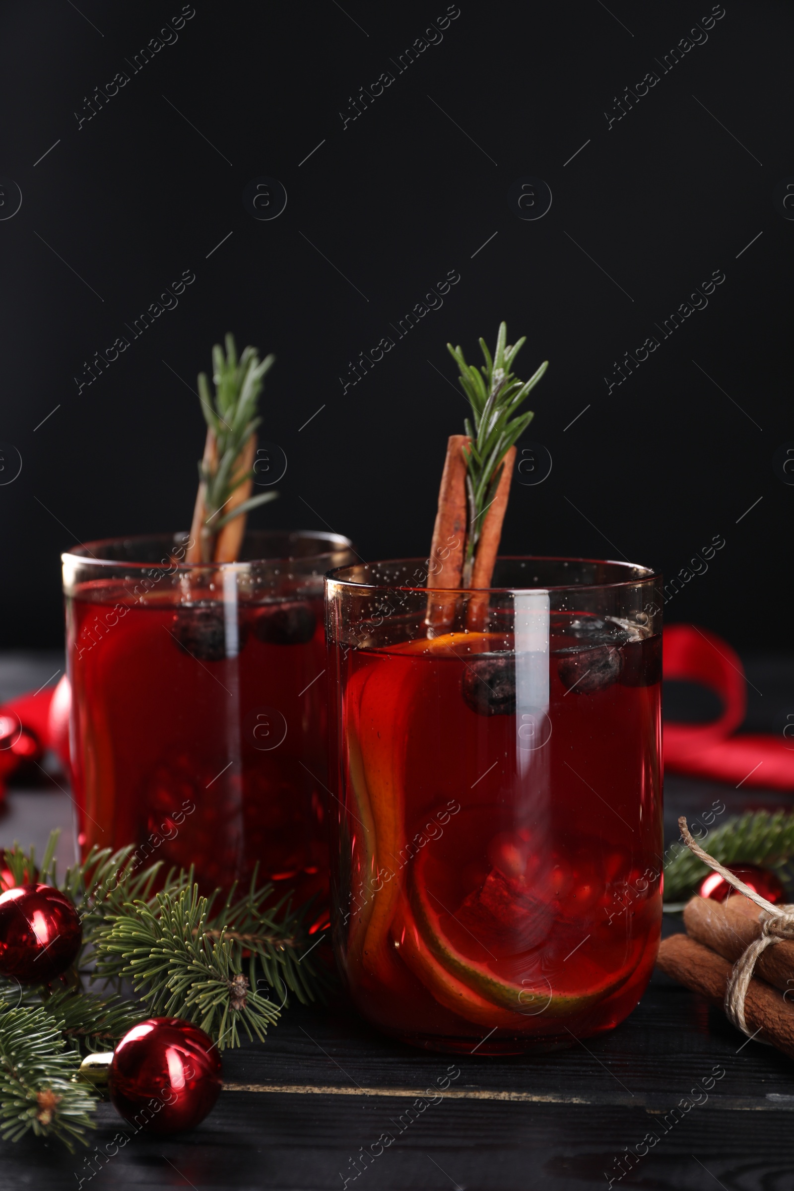 Photo of Aromatic Sangria drink in glasses, ingredients and Christmas decor on black wooden table