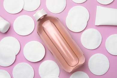 Photo of Bottle of micellar water and cotton pads on pink background, flat lay