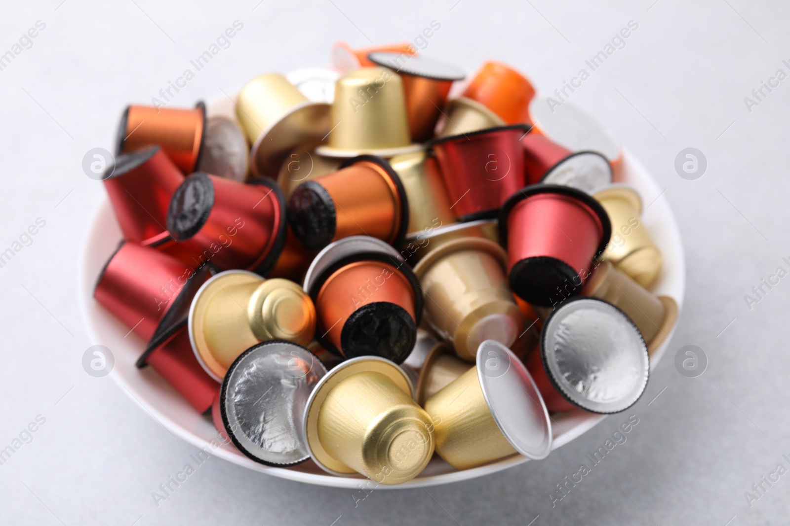 Photo of Bowl of many coffee capsules on light grey table, closeup