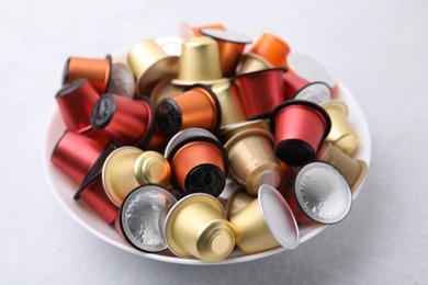 Photo of Bowl of many coffee capsules on light grey table, closeup