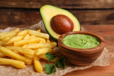 Photo of Parchment with french fries, guacamole dip, parsley and avocado served on wooden table, closeup