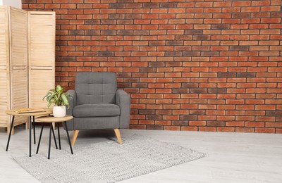 Photo of Cosy armchair and potted plant on coffee table near brick wall in room, space for text. Interior design