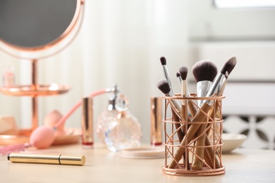 Photo of Holder with different makeup brushes on dressing table, space for text