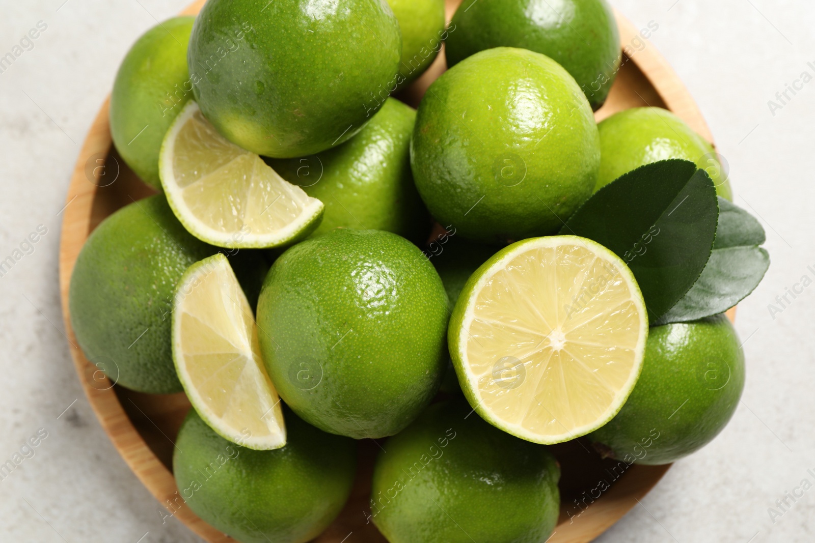 Photo of Fresh ripe limes and green leaves on light table, top view