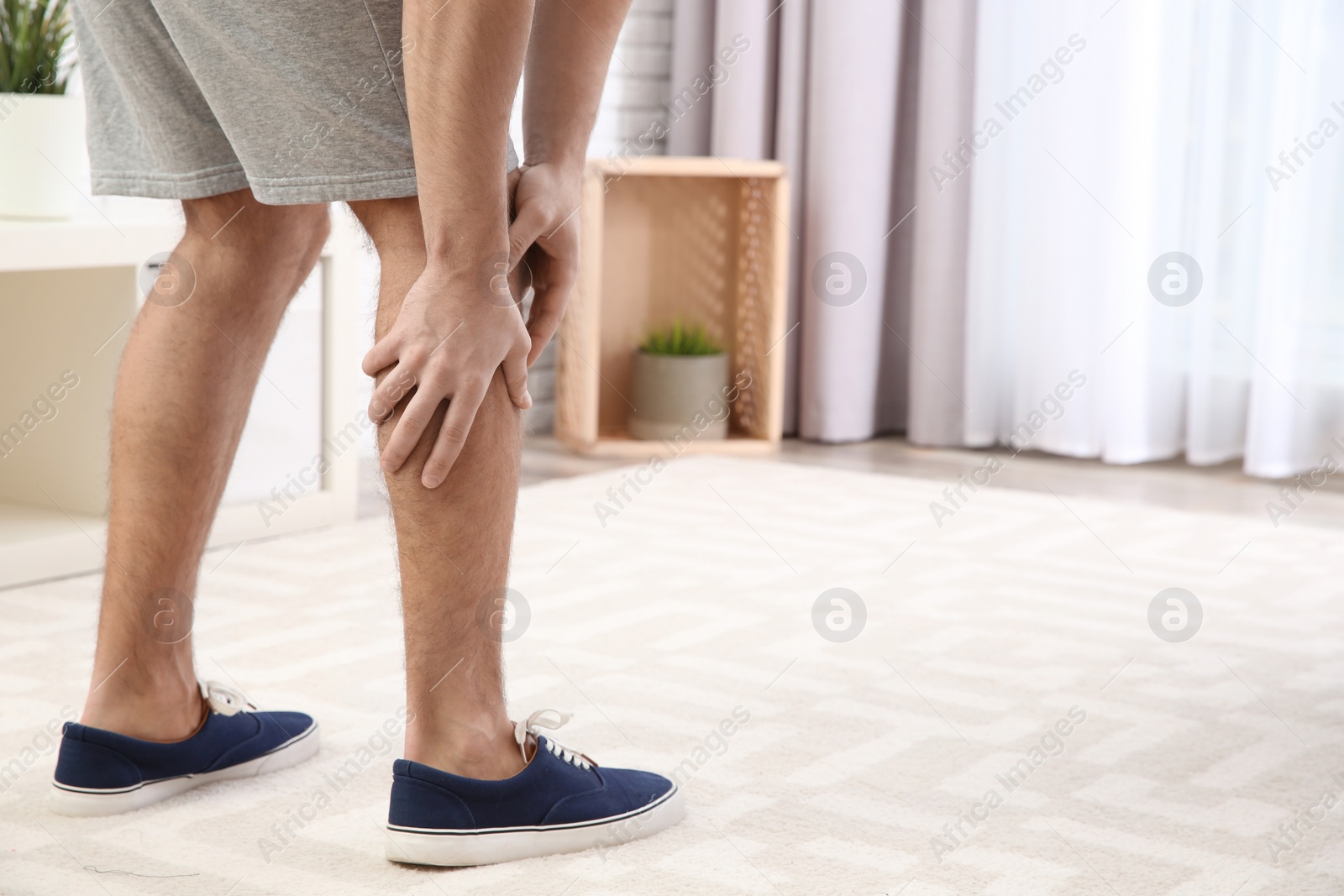 Photo of Man suffering from leg pain at home, closeup. Space for text