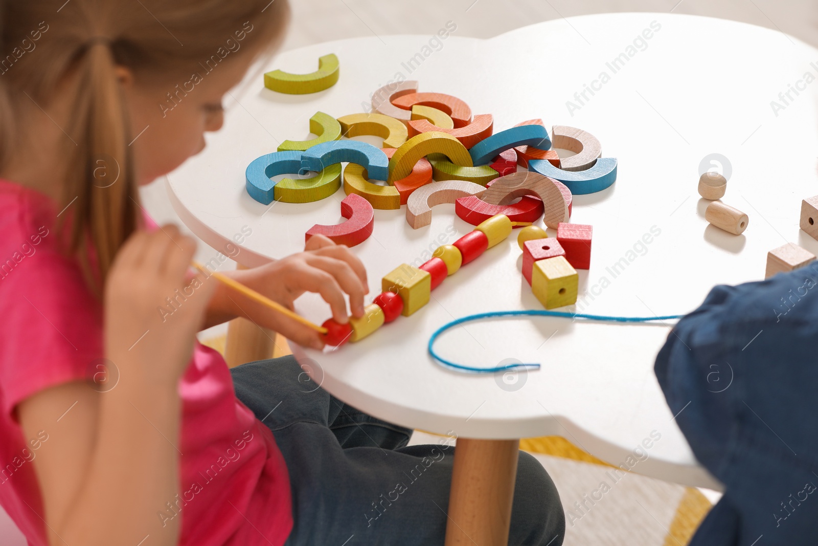 Photo of Little children playing with wooden pieces and string for threading activity at white table indoors. Developmental toys