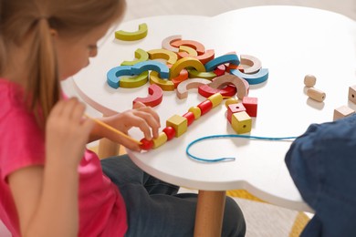 Little children playing with wooden pieces and string for threading activity at white table indoors. Developmental toys