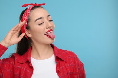 Happy woman showing her tongue on light blue background. Space for text