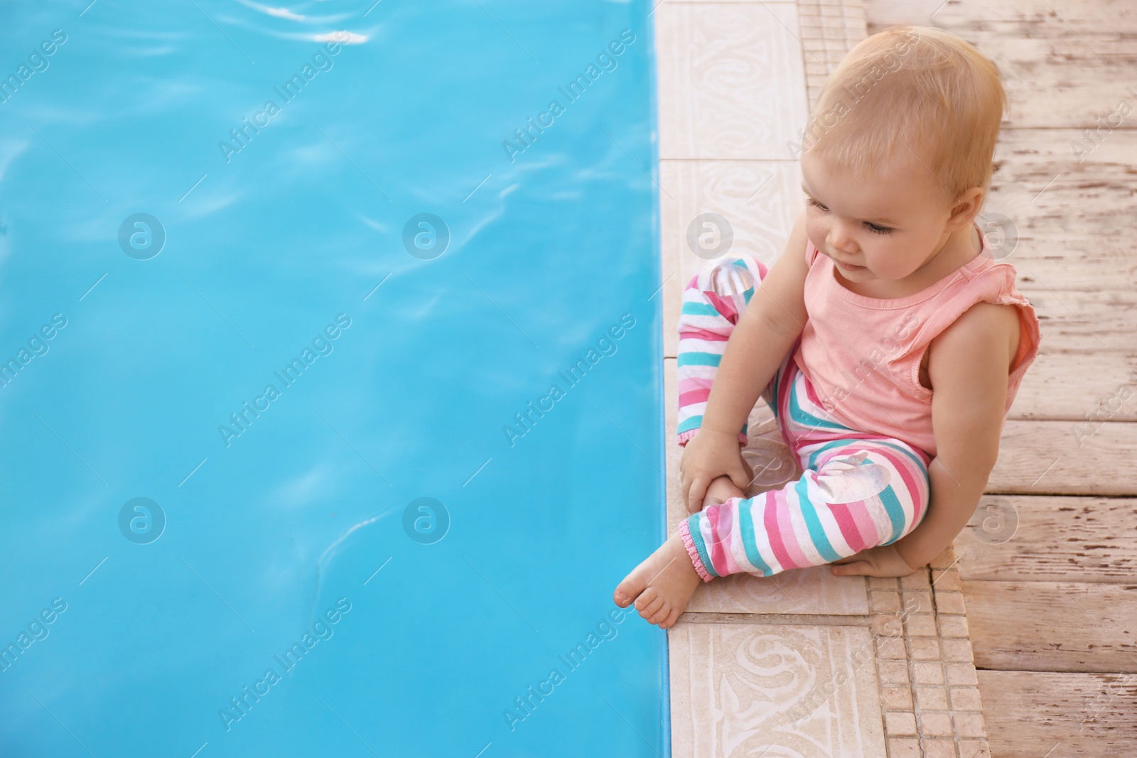 Photo of Little baby sitting near outdoor swimming pool. Dangerous situation