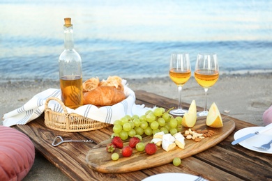 Food for picnic and white wine served on wooden pallet near river