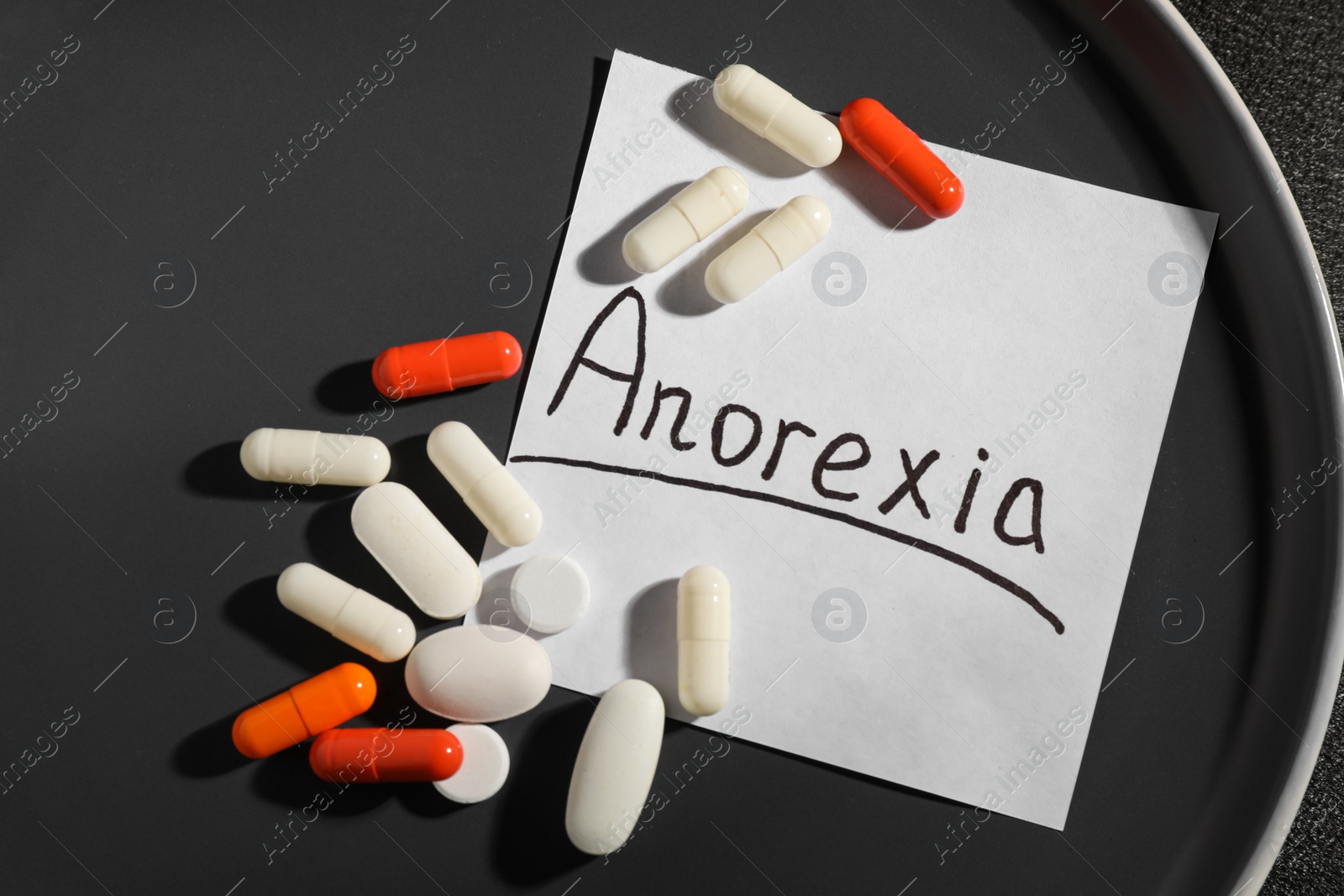 Photo of Pills and note paper with word Anorexia on grey plate, flat lay