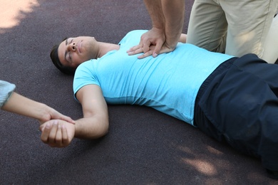 Photo of Passerby performing CPR on unconscious man outdoors. First aid