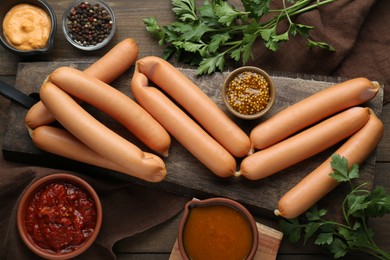 Photo of Delicious sausages, mustard, ketchup, pepper and parsley on wooden table, flat lay