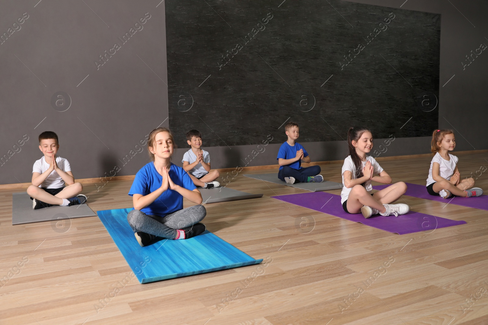 Photo of Cute little children sitting on floor and doing physical exercise in school gym. Healthy lifestyle