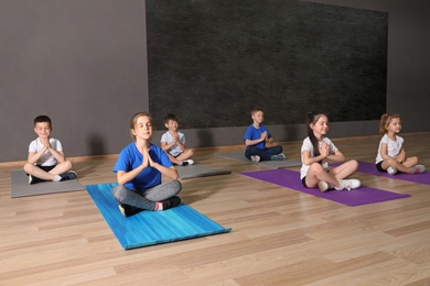 Photo of Cute little children sitting on floor and doing physical exercise in school gym. Healthy lifestyle