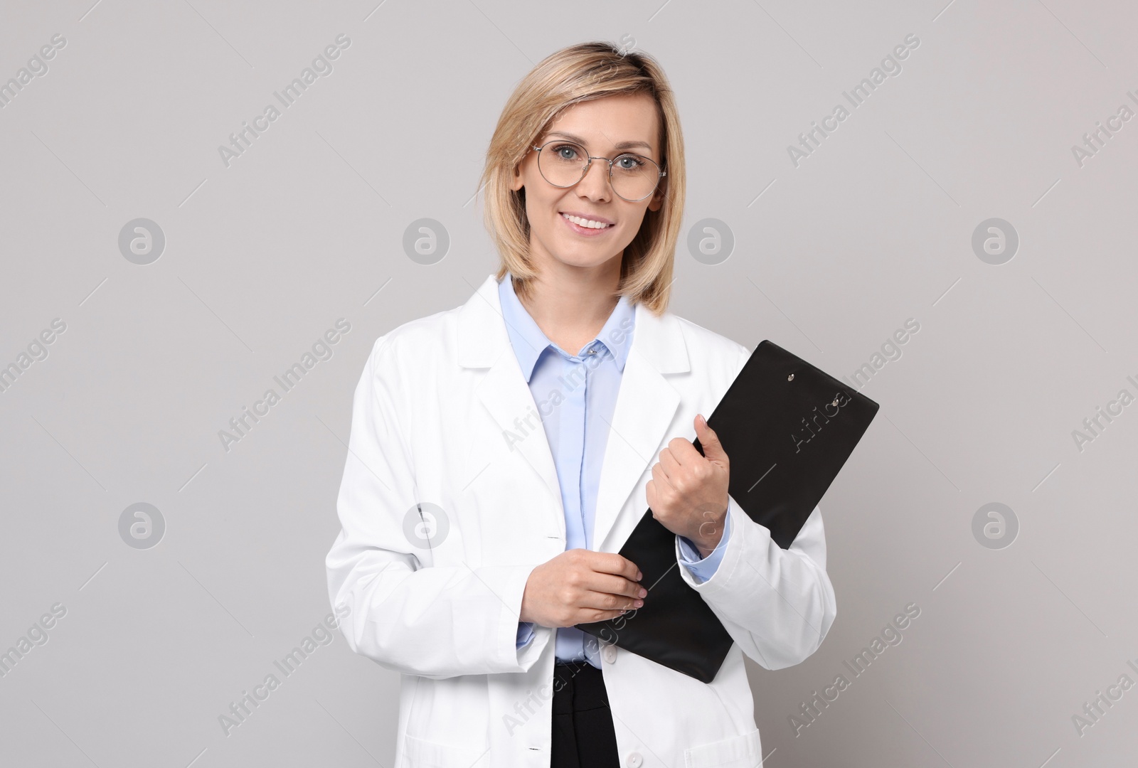 Photo of Smiling doctor with clipboard on grey background