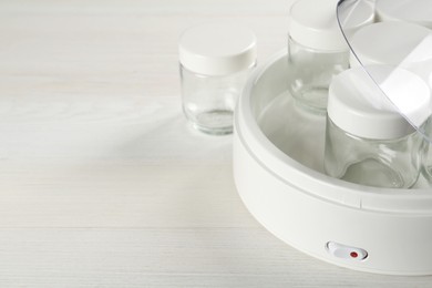 Photo of Modern yogurt maker with empty jars on white wooden table, closeup. Space for text