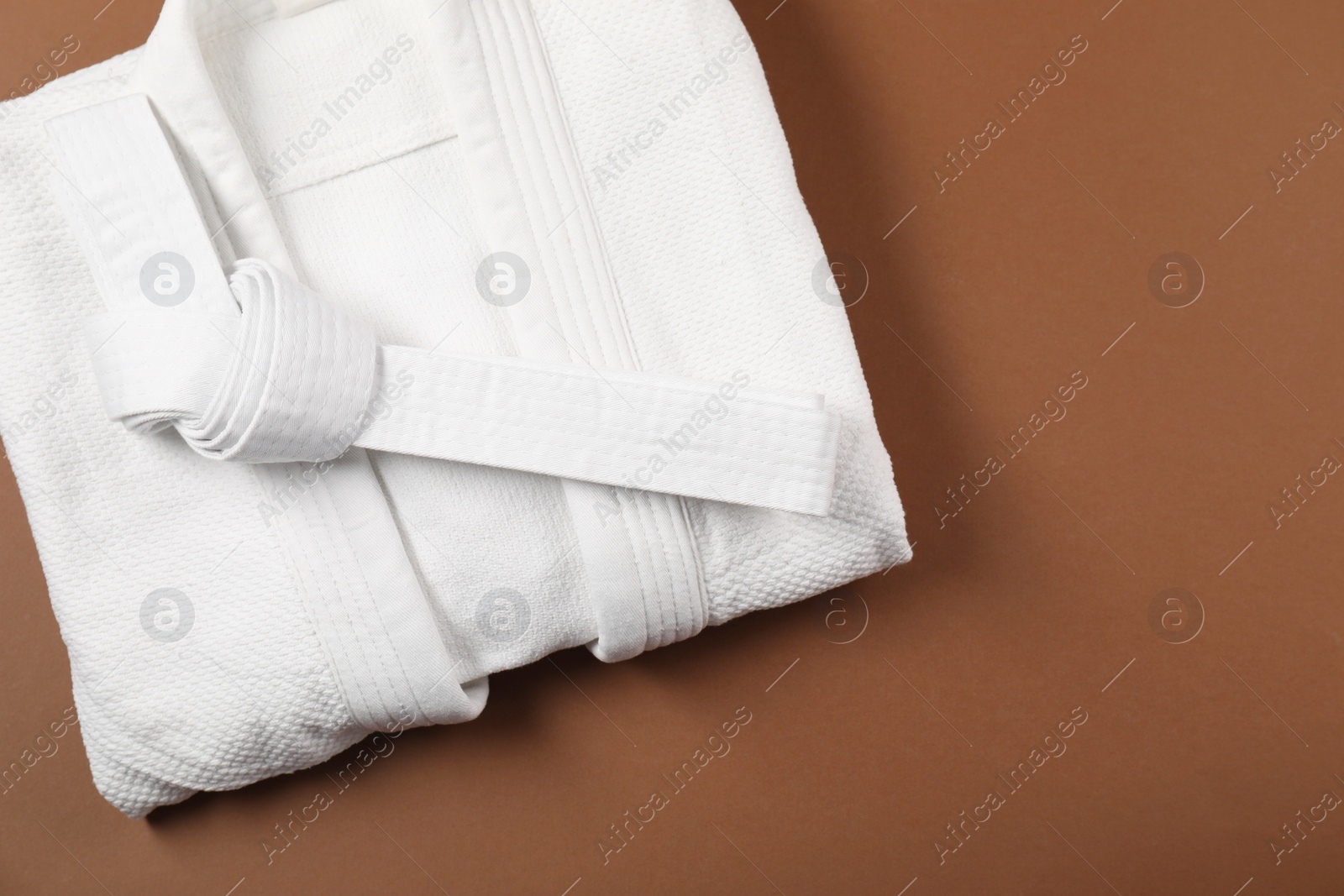 Photo of White karate belt and kimono on brown background, top view. Space for text