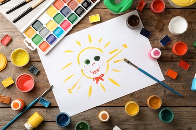 Photo of Flat lay composition with child's painting of smiling sun on table