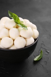 Photo of Tasty mozzarella balls and basil leaves in bowl on black table, closeup