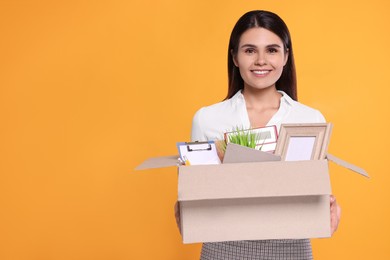 Photo of Happy unemployed woman with box of personal office belongings on orange background. Space for text