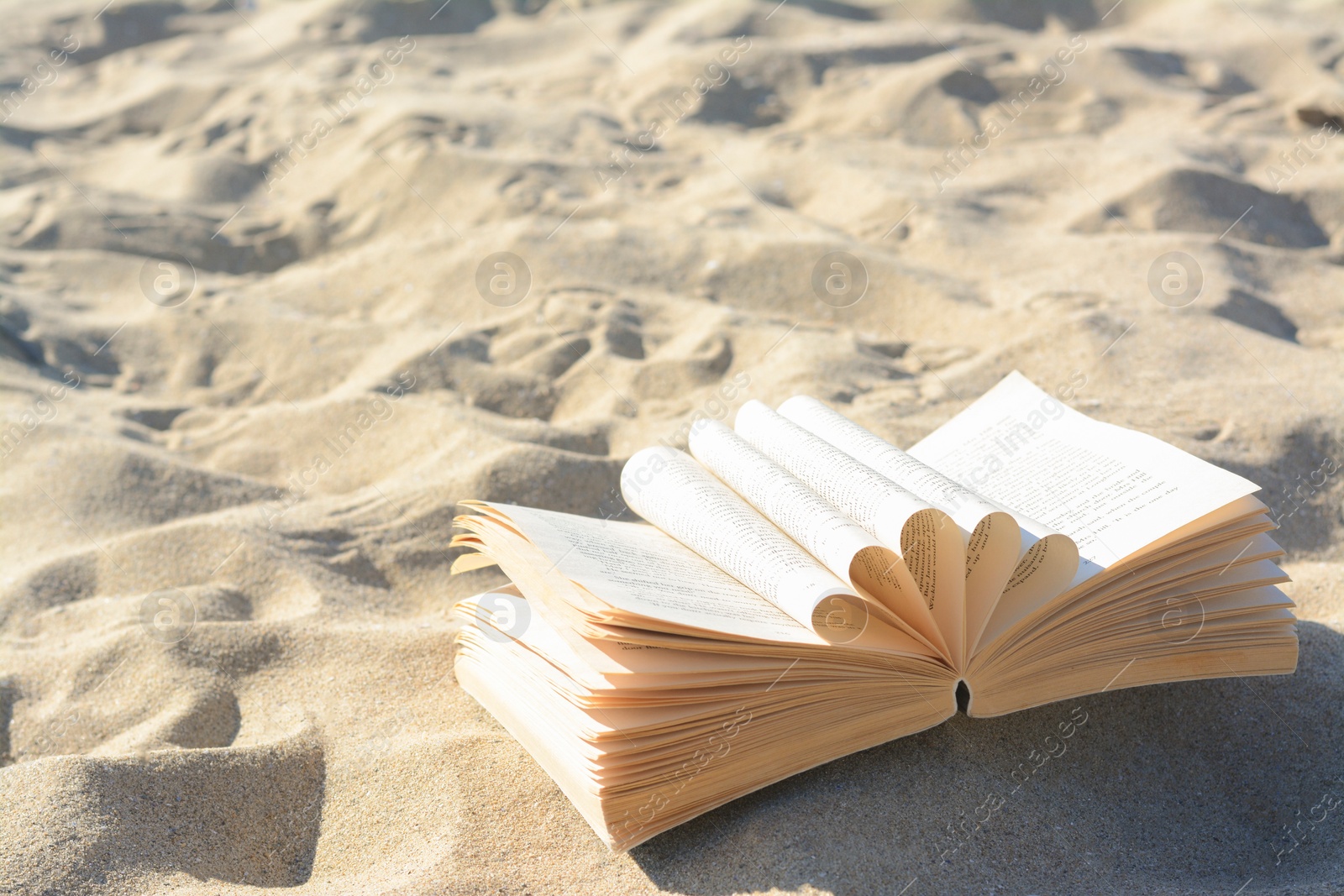 Photo of Open book on sandy beach. Space for text