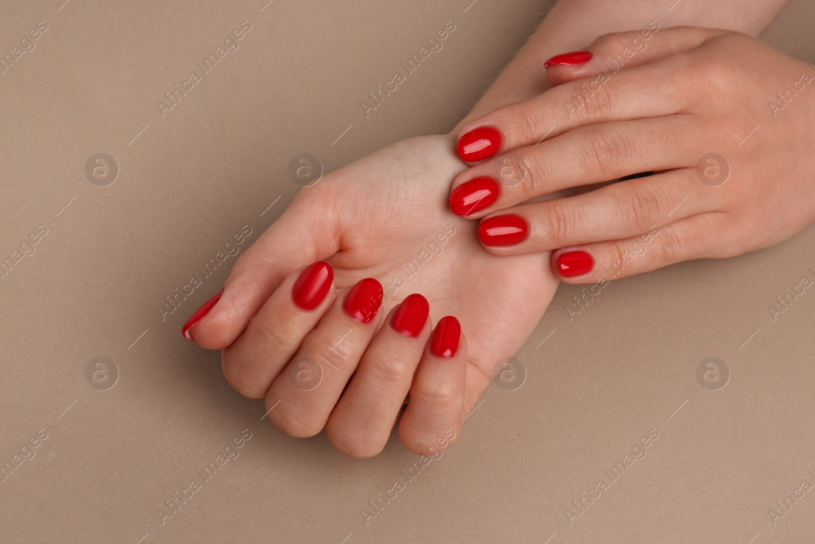Photo of Woman with red polish on nails on beige background, closeup