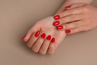 Woman with red polish on nails on beige background, closeup