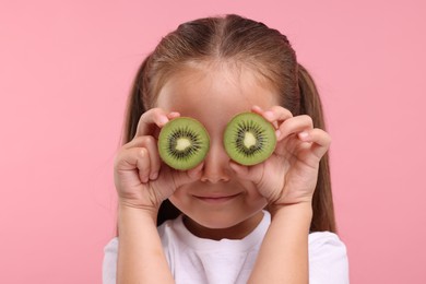 Girl covering eyes with halves of fresh kiwi on pink background