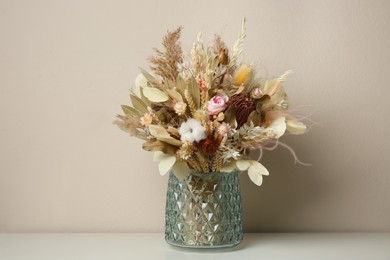 Photo of Beautiful dried flower bouquet in glass vase on white table near light grey wall