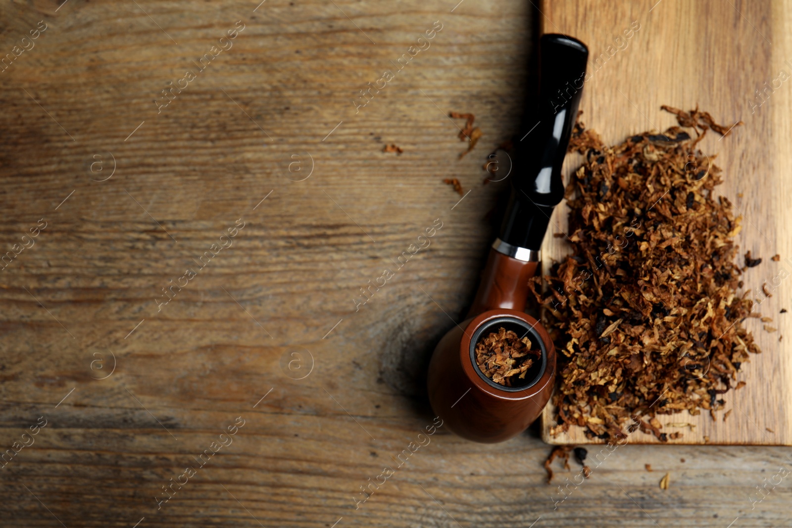 Photo of Smoking pipe and dry tobacco on wooden table, flat lay. Space for text