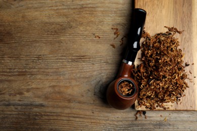 Smoking pipe and dry tobacco on wooden table, flat lay. Space for text