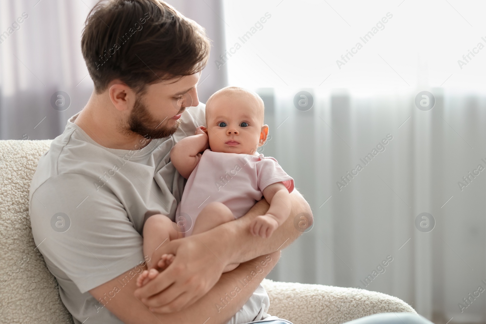 Photo of Father with his cute baby in armchair at home, space for text