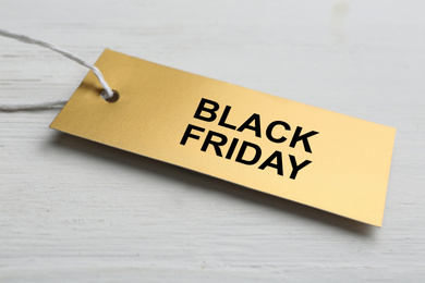Blank golden tag on white wooden background, closeup. Black Friday concept