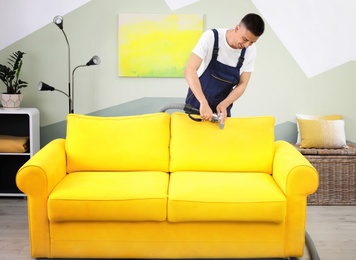 Dry cleaning worker removing dirt from sofa indoors