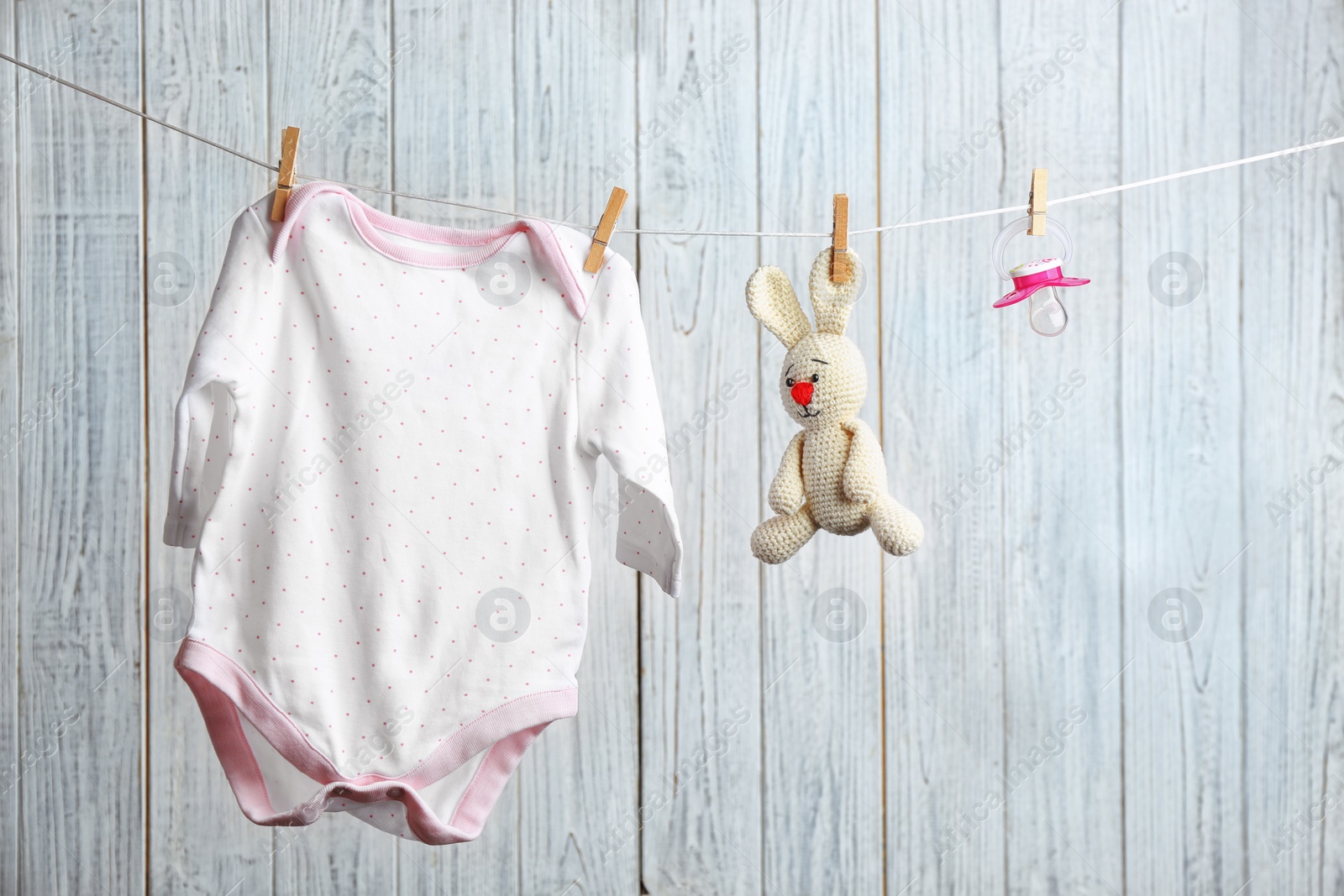 Photo of Bodysuit, pacifier and toy bunny on laundry line against wooden background. Baby accessories