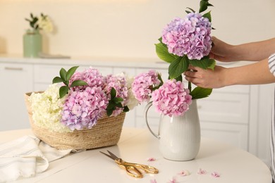 Photo of Woman making bouquet with beautiful hydrangea flowers at table indoors, closeup. Interior design element