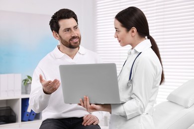 Photo of Doctor with laptop consulting patient during appointment in clinic