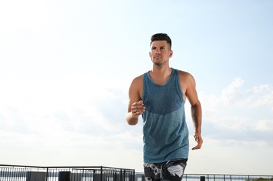 Photo of Handsome man in sportswear running outdoors on sunny day